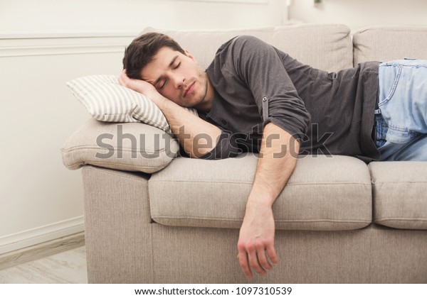 昼間は自宅のソファで寝るカジュアルな若い男性 の写真素材 今すぐ編集
