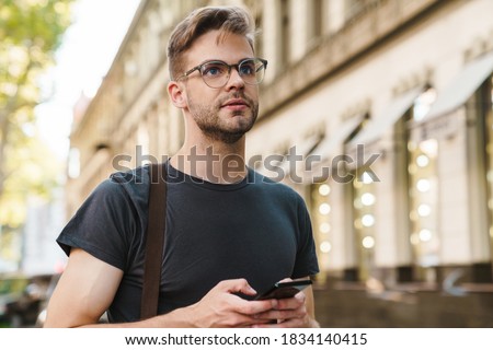 Young casual man using smart phone texting messages in the street