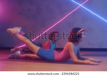 Young caucasian and african american woman doing leg lift exercise on floor at studio