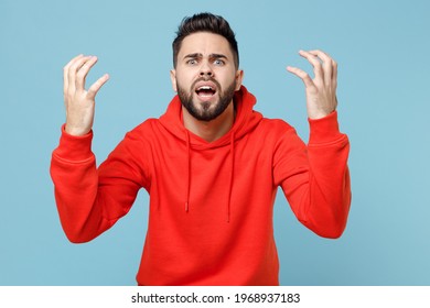 Young caucasian angry indignant nervous irritated stressed bearded man 20s wearing casual red orange hoodie spreading hands isolated on blue color background studio portrait People lifestyle concept