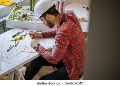 Young Caucasian Architect Studying A Floor Plan, A Serious Civil Engineer Working With Documents, Drawings And Building Models. Isolated In Office