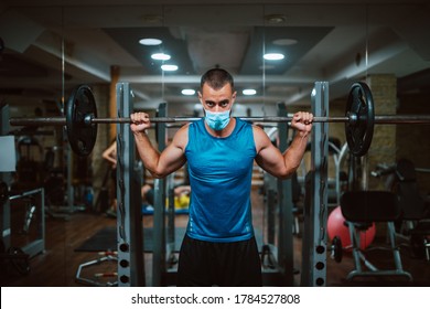 A Young Caucasian Athlete Man With A Mask On His Face Exercises And Lifts Dumbbel In The Gym. COVID 19 Coronavirus Protection