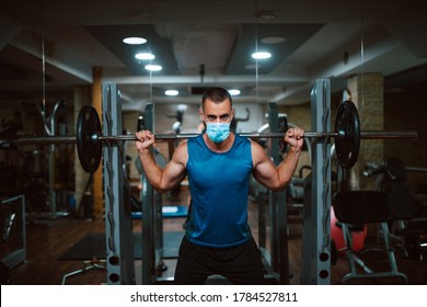 A Young Caucasian Athlete Man With A Mask On His Face Exercises And Lifts Dumbbel In The Gym. COVID 19 Coronavirus Protection