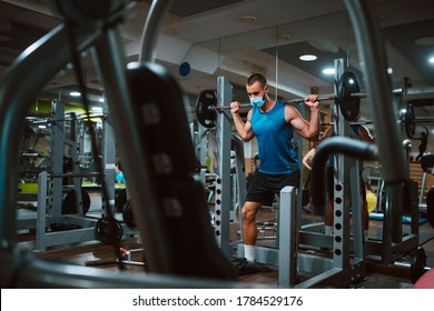 A Young Caucasian Athlete Man With A Mask On His Face Exercises And Lifts Dumbbel In The Gym. COVID 19 Coronavirus Protection