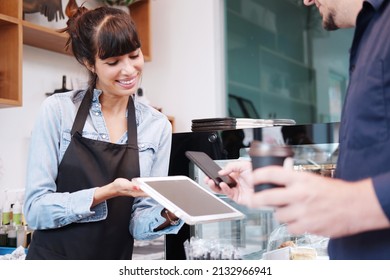 Young Caucasian barista woman is holding tablet for customer using smart phone scan QR code on tablet for payment at counter bar at coffee shop. Technology of digital pay without money concept. - Shutterstock ID 2132966941