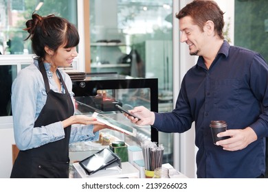 Young Caucasian barista woman is holding tablet for customer using smart phone scan QR code on tablet for payment at counter bar at coffee shop. Technology of digital pay without money concept. - Shutterstock ID 2139266023
