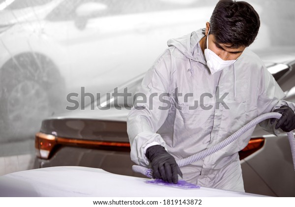 young caucasian bearded car cleaner in respirator\
and protective glasses polishing car with polish machine, in\
uniform. isolated in car\
service