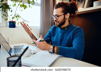 Young Caucasian Bearded Engineer Sitting In His Office, Holding Windmill Model And Thinking What How Redesign It. Sustainable Concept.