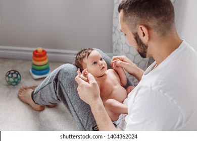 Young Caucasian bearded father holding newborn baby on laps knees. Male man parent rocking talking to child daughter son. Authentic lifestyle documentary moment. Single dad family life.