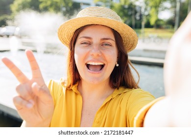 Young Caucasian Beautiful Woman In Straw Hat Gesturing Peace Sign On Urban Background, Summer Time. Number Two. Happy Redhead Girl Take A Selfie At Vacation. Solo Female Traveler.