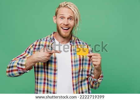 Young caucasian blond man with dreadlocks he wear casual shirt hold in hand point finger on mock up of credit bank card isolated on pastel plain light green background studio. People lifestyle concept