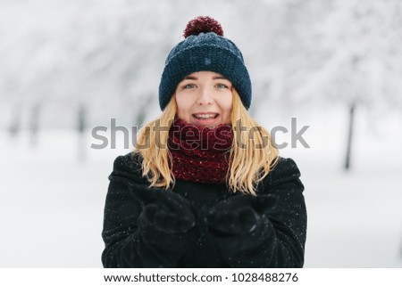 Young caucasian blonde girl in black coat and red knitted scarf walks in winter park