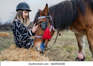 Young Caucasian Blonde Woman Female Girl Pet And Play With The Horse Riding In Nature Wearing Helmet In Winter Or Autumn Day Against A Cloudy Sky In The Field - Freedom Friendship Concept Copy Space