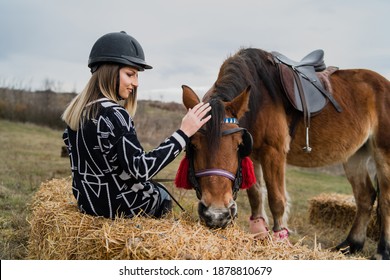 Young Caucasian Blonde Woman Female Girl Pet And Play With The Horse Riding In Nature Wearing Helmet In Winter Or Autumn Day Against A Cloudy Sky In The Field - Freedom Friendship Concept Copy Space