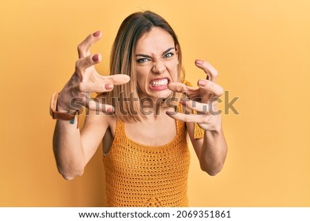 Young caucasian blonde woman wearing casual yellow t shirt shouting frustrated with rage, hands trying to strangle, yelling mad 