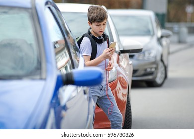 Young Caucasian Boy Is Busy With His Mobile Smart Phone Not Paying Attention To The Danger Of Traffic In The Street