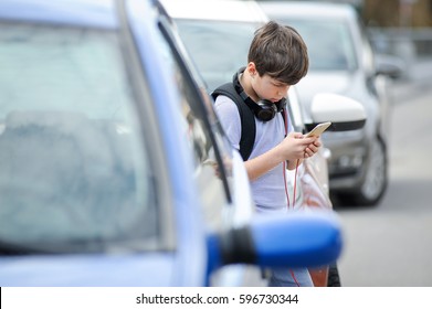 Young Caucasian Boy Is Busy With His Mobile Smart Phone Not Paying Attention To The Danger Of Traffic In The Street