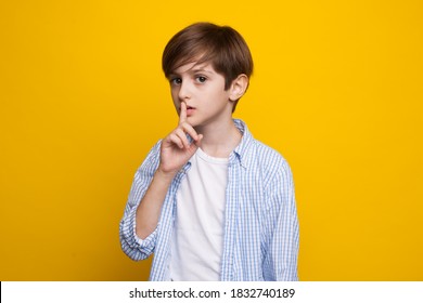 Young caucasian boy is gesturing the silence soung posing serious on a yellow studio wall in casual clothes