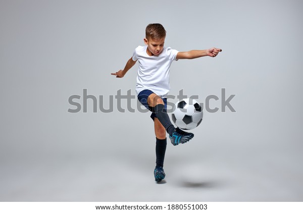 young caucasian\
boy with soccer ball doing flying kick isolated in studio, athletic\
sportive boy in uniform