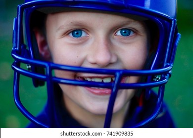 A young Caucasian boy wearing a football helmet and smiling. Helmet purple, eyes and shirt blue. Teeth growing in from losing baby teeth.  - Powered by Shutterstock