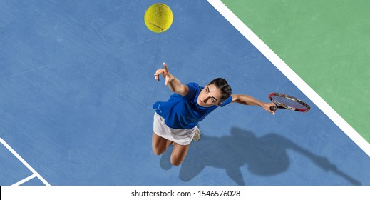 Young Caucasian Brunette Woman In Blue Shirt Playing Tennis At The Court. Hits Ball With Racket, Outdoors. Youth, Flexibility, Power, Energy. Copyspace. Top View. Motion, Action, Healthy Lifestyle.