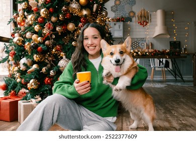 Young caucasian brunette woman looking at the camera sitting with corgi dog by christmas tree at home. High quality photo - Powered by Shutterstock