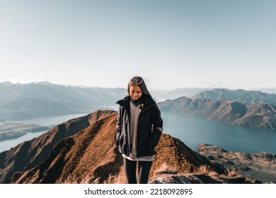 young caucasian brunette woman wearing black jacket gray sweater black pants looking at the ground s and smiling from the top of a mountain with her hands in the pockets of her black jacket - Shutterstock ID 2218092895