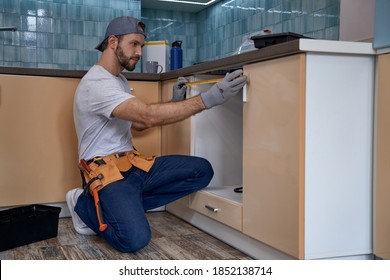 Young caucasian builder with measuring tape near kitchen drawer