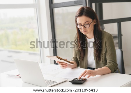 Young caucasian business woman counting funds, planning budget, paying bills online using calculator. Freelancer boss CEO doing paperwork with finances.