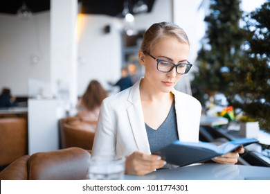young caucasian business woman with glasses looks at a diary at a cafe