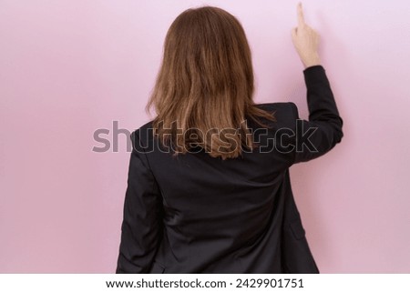 Young caucasian business woman wearing black jacket posing backwards pointing ahead with finger hand 