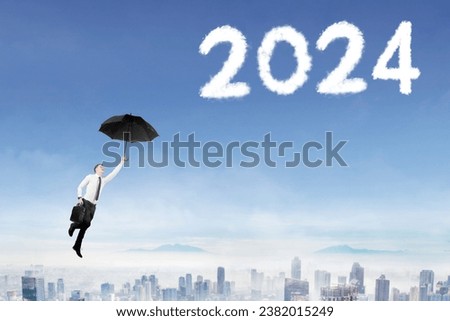 Young caucasian businessman holding an umbrella while flying in the blue sky reaching number 2024