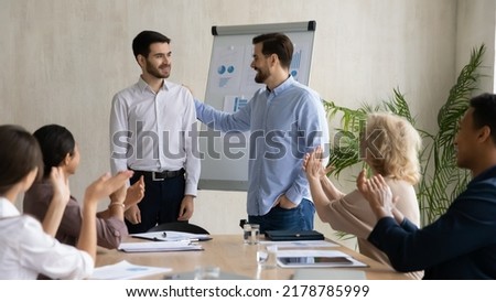 Young Caucasian businessman introduce new male employee or worker at group meeting in office. Man boss or director welcome newcomer newbie at workplace. Colleagues applaud. Recruitment concept.