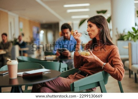 A young Caucasian businesswoman is in the office cafeteria eating her lunch on her break.