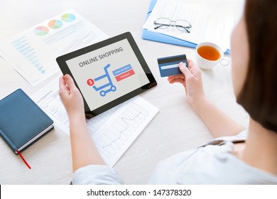 Young caucasian businesswoman sitting at the desk in the office and using credit card and modern digital tablet for online shopping - Powered by Shutterstock