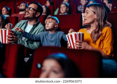 A young Caucasian child is with it's parent's in a movie theater watching a mocie and eating popcorn. - Shutterstock ID 2269061071