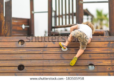 Young caucasian child playing on the playground, climbing on the wooden wall