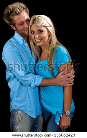Young Caucasian Couple in blue shirts and jeans embracing. Shot on a black background.