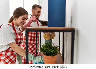 Young caucasian couple cleaning dust using duster at home.