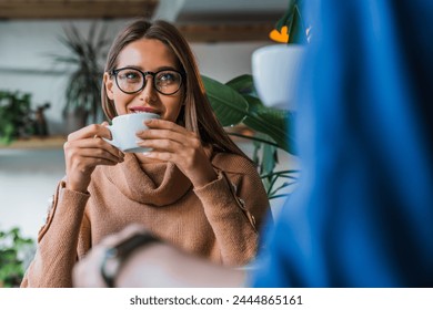 Young caucasian couple coworkers partners drinking coffee in cozy loft coffee shop with green plans on background. Happy cheerful man and woman in cafe, having a great time together. Business meeting - Powered by Shutterstock