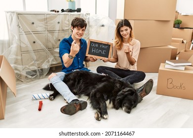 Young Caucasian Couple With Dog Holding Our First Home Blackboard At New House Beckoning Come Here Gesture With Hand Inviting Welcoming Happy And Smiling 