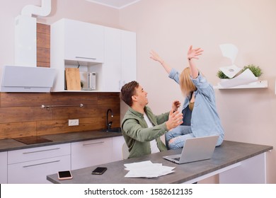 young caucasian couple happy and cheerful together in kitchen, using laptop, papers on table. sit together with raised hands - Shutterstock ID 1582612135