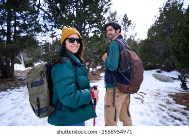 Young caucasian couple hiking together in a snowy forest, turning to look at the camera smiling during winter holidays. Image with copy space. - Powered by Shutterstock