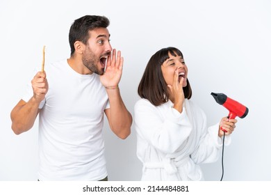 Young Caucasian Couple Holding A Hairdryer And Toothbrush Isolated On White Background Shouting With Mouth Wide Open To The Lateral