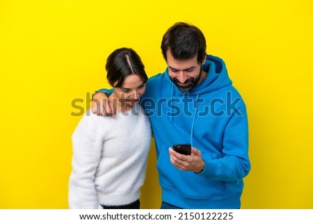 Young caucasian couple isolated on yellow background sending a message or email with the mobile