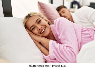 Young Caucasian Couple Lying On The Bed. Woman Smiling And Looking To The Camera At Home.