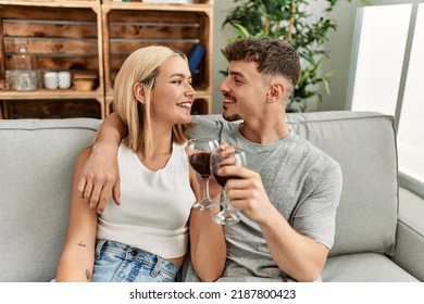 Young Caucasian Couple Smiling Happy Toasting With Red Wine At Home.