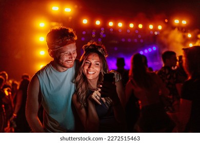 A young Caucasian couple is taking a selfie at a concert, smiling and wearing casual party clothes - Powered by Shutterstock