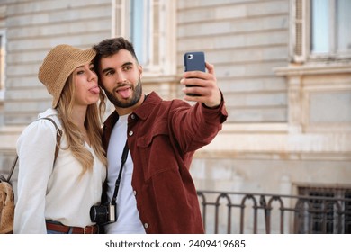 Young Caucasian couple taking a selfie stick out tongue while sightseeing the city of Madrid, Spain.