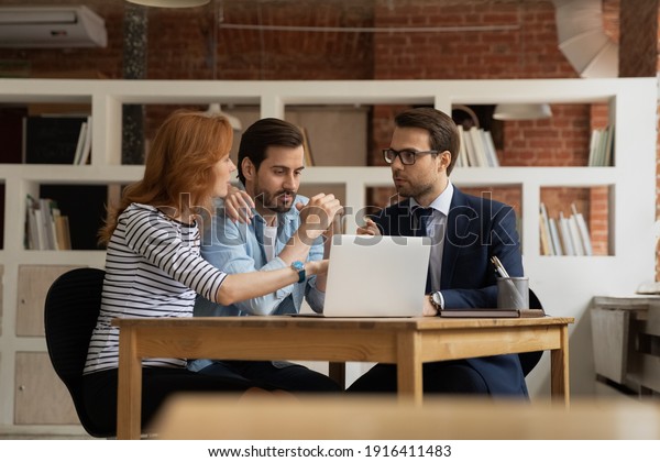 Young Caucasian couple talk consult with male\
realtor or broker at meeting in office. Man real estate agent have\
consultation with spouses, discuss house rent or bank loan. Realty,\
rental concept.